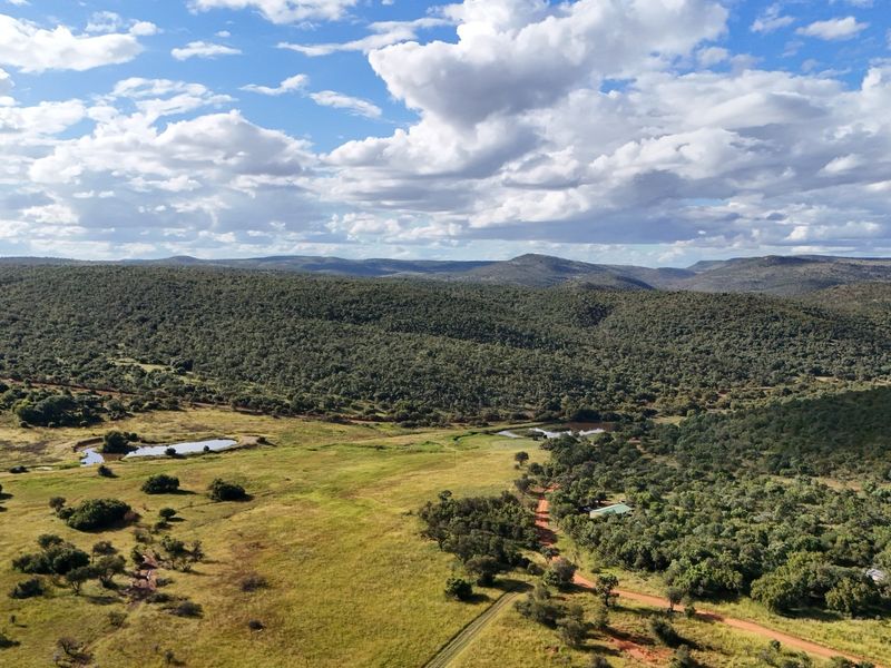 An aerial view of a vast, undeveloped residential land parcel featuring rolling hills, natural vegetation, dirt access roads, and small water dams.