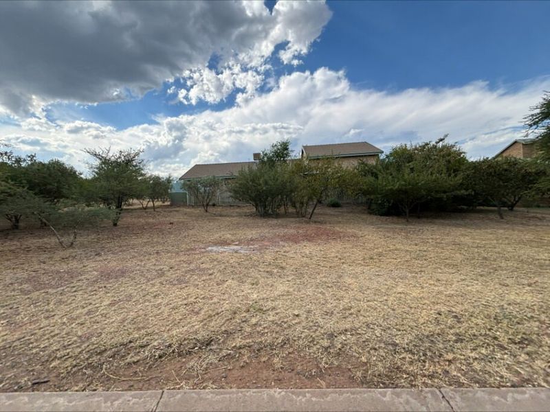 A view of the rear yard area featuring dry grass, established trees, perimeter fencing, and a water tank.