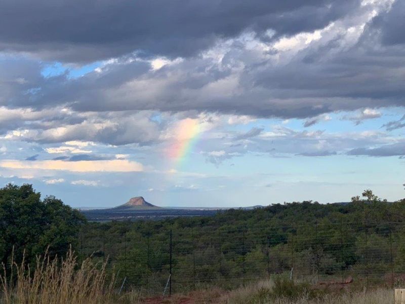 A scenic landscape view featuring natural terrain, distant hills, and a rainbow under a cloudy sky, captured from the property boundary.