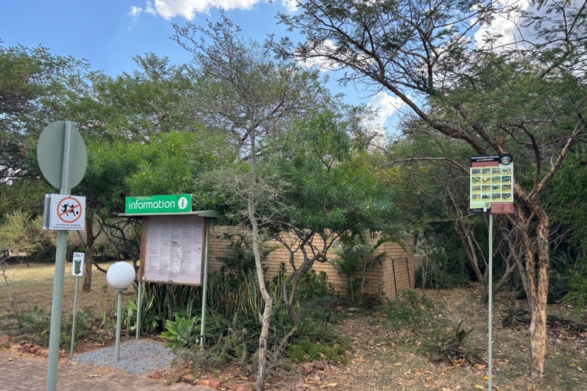 A landscaped garden area featuring a brick wall, paved walkway, and informational signage within a residential estate setting.