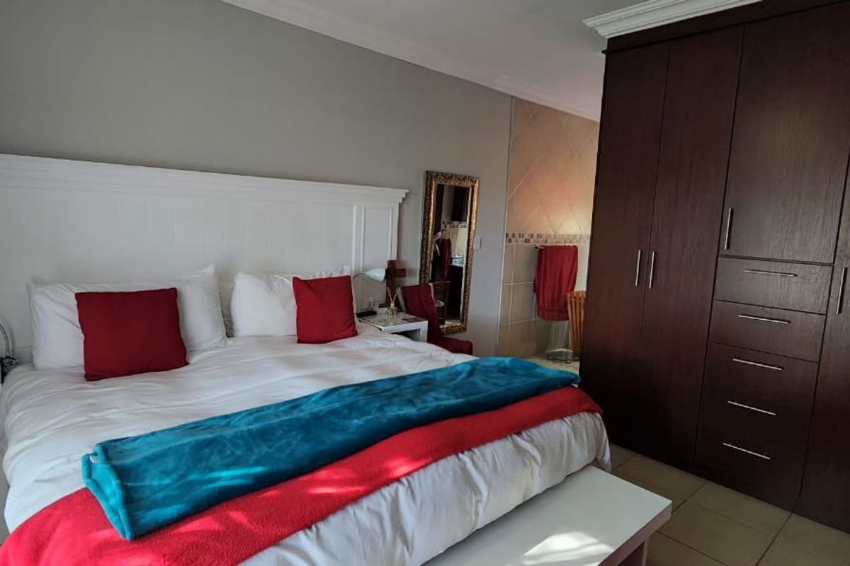 A well-maintained bedroom featuring a large built-in dark wood wardrobe, a white headboard, and an en-suite bathroom area with tiled finishes.