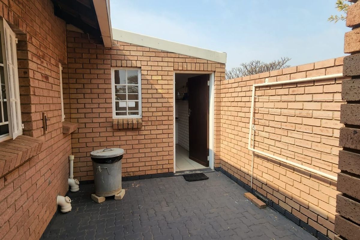 A private exterior courtyard area featuring paved flooring, face-brick walls, and a wall-mounted drying rack, providing access to the utility or kitchen entrance.
