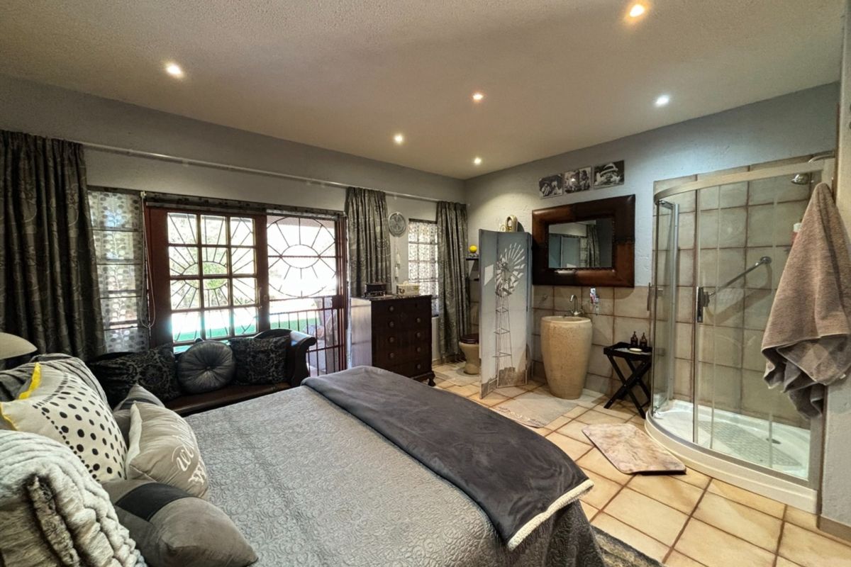 Spacious bedroom featuring an integrated en-suite bathroom with a glass shower enclosure, stone basin, and direct access to an outdoor patio area.