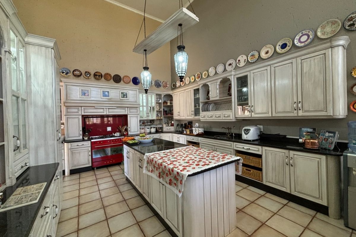 Spacious farmhouse kitchen featuring custom cabinetry, a central island with granite countertops, and a prominent red range cooker under high vaulted ceilings.