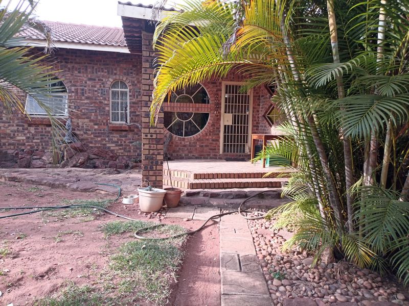 Rear exterior view of a face-brick home featuring arched windows, a circular feature window, and a paved patio area with steps.