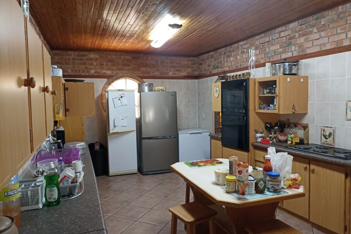 A spacious kitchen featuring exposed brick walls, a wooden ceiling, built-in wooden cabinetry, and tiled flooring, offering a functional layout with ample storage.