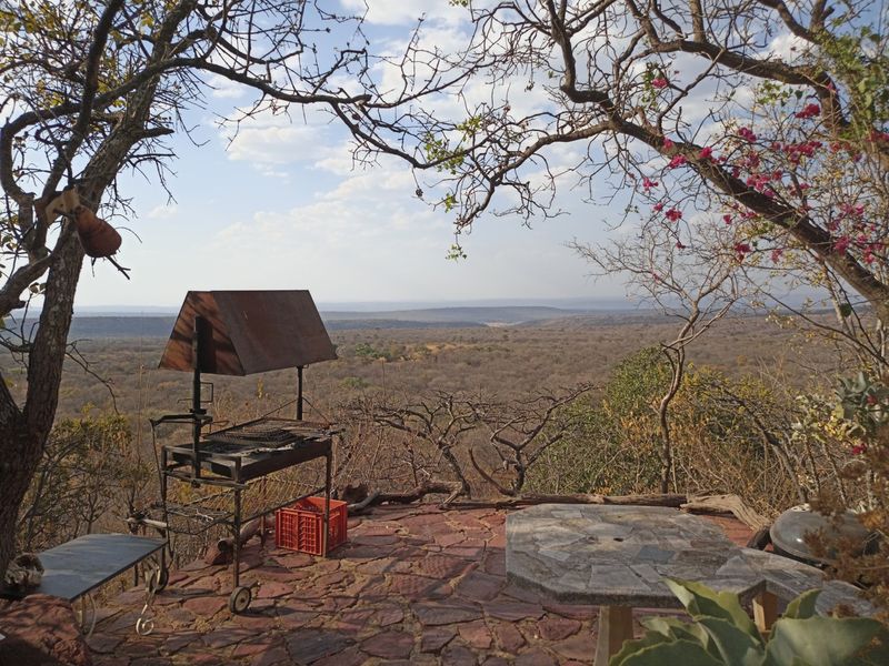 An elevated outdoor viewing area featuring a stone-paved patio and a built-in braai, offering expansive panoramic views of the surrounding landscape.