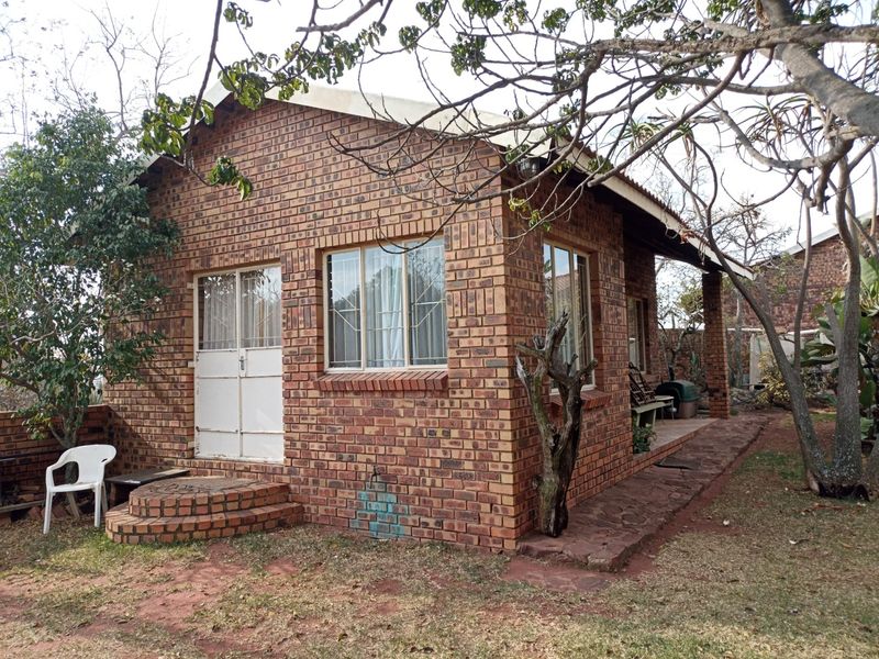 A detached face brick building featuring a covered patio, brick steps, and secure entrance, set within a garden environment.