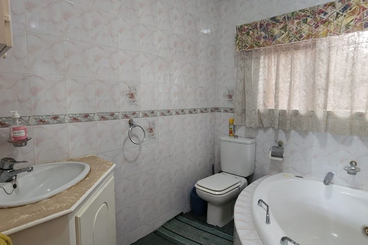 A functional bathroom featuring a corner bathtub, a vanity basin with storage, and a toilet, finished with classic wall tiling.