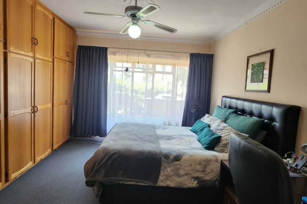 Spacious bedroom featuring extensive built-in wooden cabinetry, a ceiling fan, and large windows allowing for natural light.