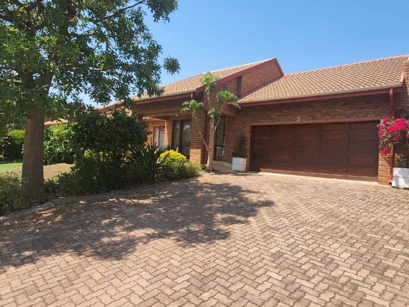 A well-maintained townhouse featuring a face-brick exterior, a paved driveway, and a secure wooden garage door, set within a landscaped garden.