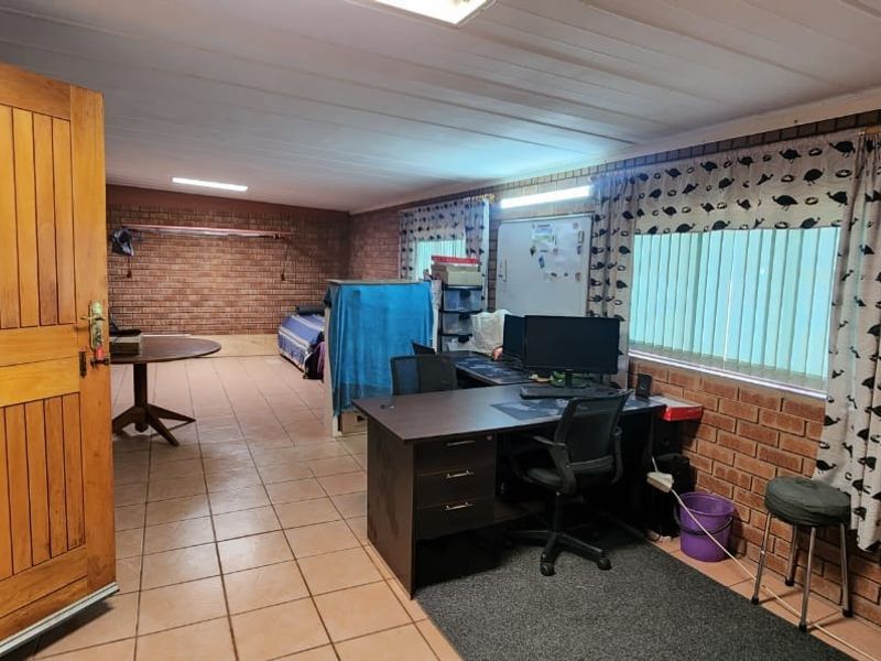 Spacious open-plan room featuring exposed brick walls, tiled flooring, and large windows, suitable for a versatile living area, home office, or studio space.