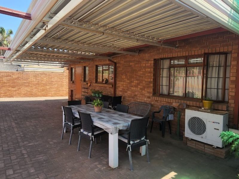 A covered outdoor patio area featuring brick walls, paved flooring, and a corrugated metal roof structure, suitable for outdoor dining and relaxation.