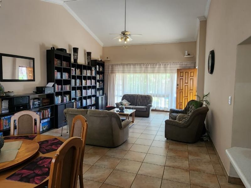 Open-plan living and dining area featuring tiled flooring, vaulted ceilings, and a ceiling fan, with direct access to the outdoor patio area.