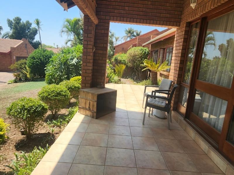 A covered brick patio featuring tiled flooring, providing a pleasant outdoor space overlooking the garden and surrounding townhouse complex.