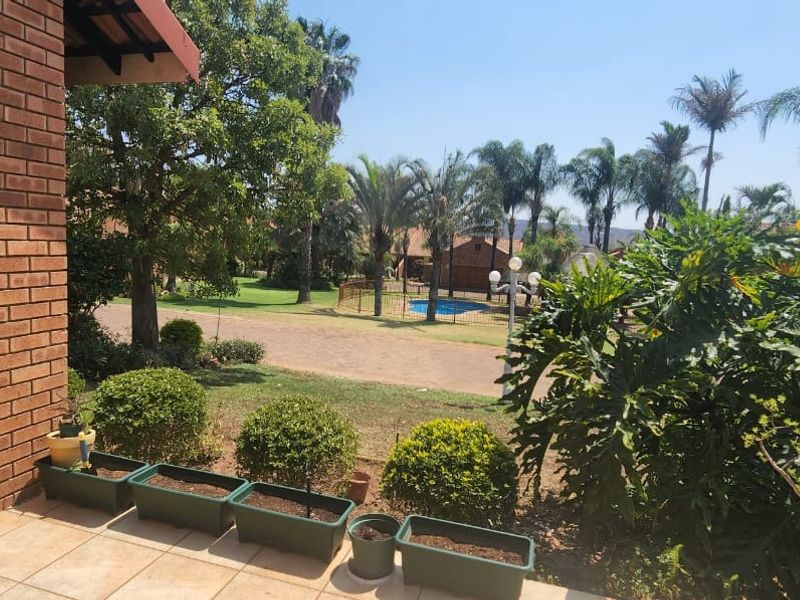 A view from a covered patio overlooking a landscaped garden area with a swimming pool and established trees in a residential complex.