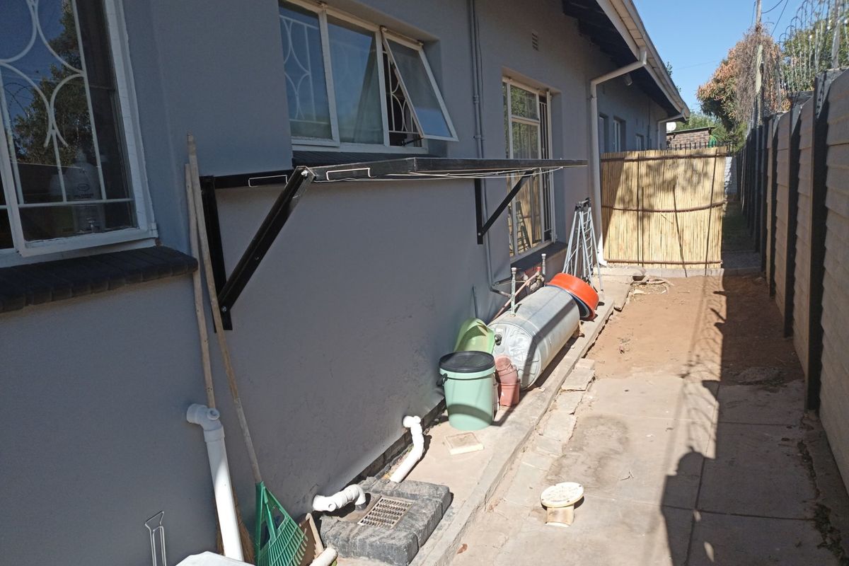 Side exterior area of the apartment featuring a wall-mounted drying rack, drainage point, and paved walkway along the building perimeter.
