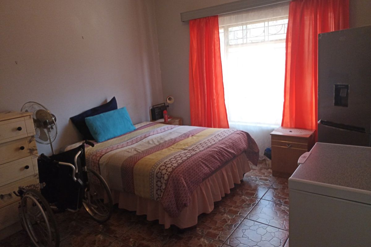 A bedroom featuring tiled flooring and a large window with curtain tracks, providing natural light to the space.