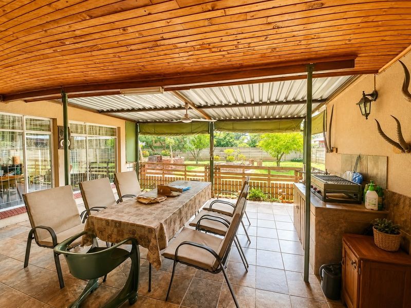 Covered outdoor patio featuring a timber ceiling, tiled flooring, and a built-in braai area, overlooking the rear garden.