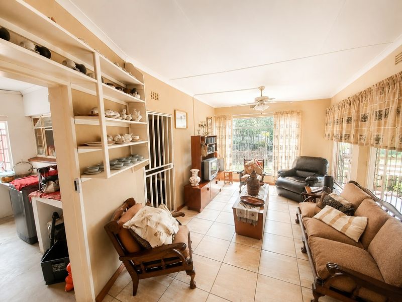 Open plan living area featuring tiled floors, a ceiling fan, and built-in shelving, with an adjacent kitchen area visible.
