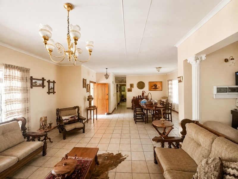 Spacious open-plan living and dining area featuring ceramic tile flooring, a decorative column, and a classic chandelier, offering a versatile layout.