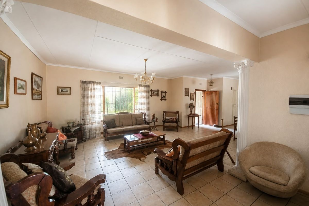Spacious living area featuring ceramic tile flooring, a decorative column, and natural light through a large window with security bars.