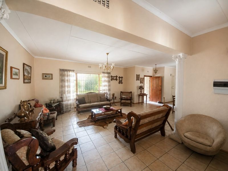 Spacious living area featuring ceramic tile flooring, a decorative column, and natural light through a large window with security bars.