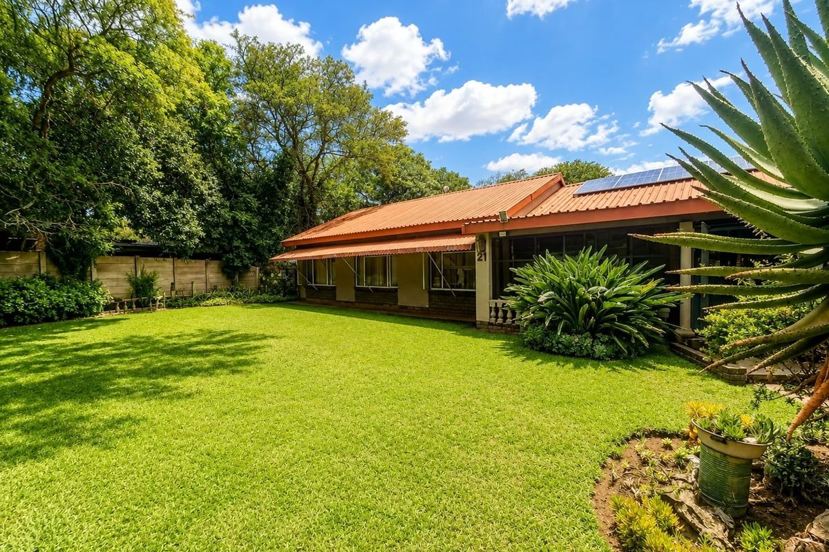 A well-maintained rear garden featuring a lush lawn, mature landscaping, and a house exterior equipped with solar panels and protective window awnings.