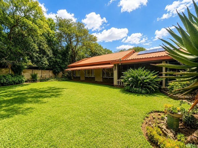A well-maintained rear garden featuring a lush lawn, mature landscaping, and a house exterior equipped with solar panels and protective window awnings.