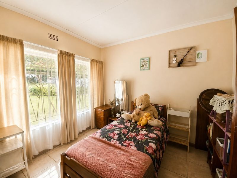 A bedroom featuring tiled flooring and large windows with security bars, providing natural light and a view of the garden.