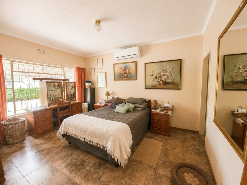 A well-lit bedroom featuring tiled flooring, an installed air conditioning unit, and large windows with security bars.