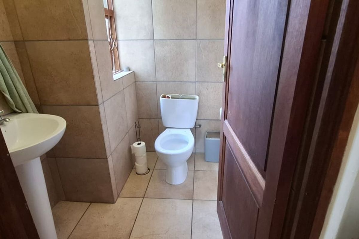 A compact bathroom featuring a pedestal basin and a toilet with tiled walls and flooring.