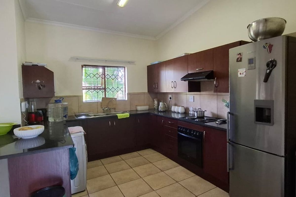 A functional kitchen featuring dark wood cabinetry, granite countertops, a built-in oven with extractor fan, and tiled flooring.