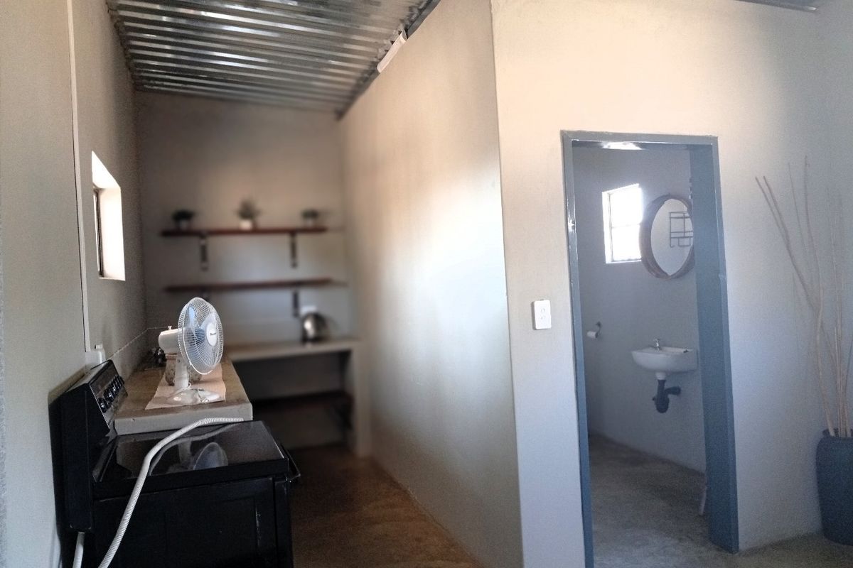 A rustic kitchen area featuring a corrugated metal ceiling, concrete countertops, and an adjoining small bathroom with a wall-mounted basin.