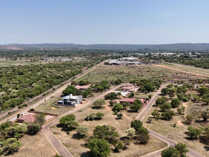 An aerial view of a residential development area featuring paved roads, established plots, and surrounding natural landscape.