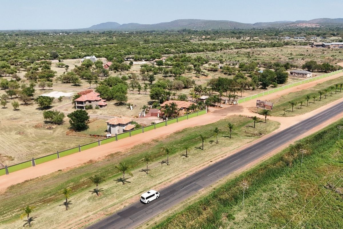 Aerial view of a residential vacant land plot featuring perimeter fencing and direct access to a paved main road in a rural setting.