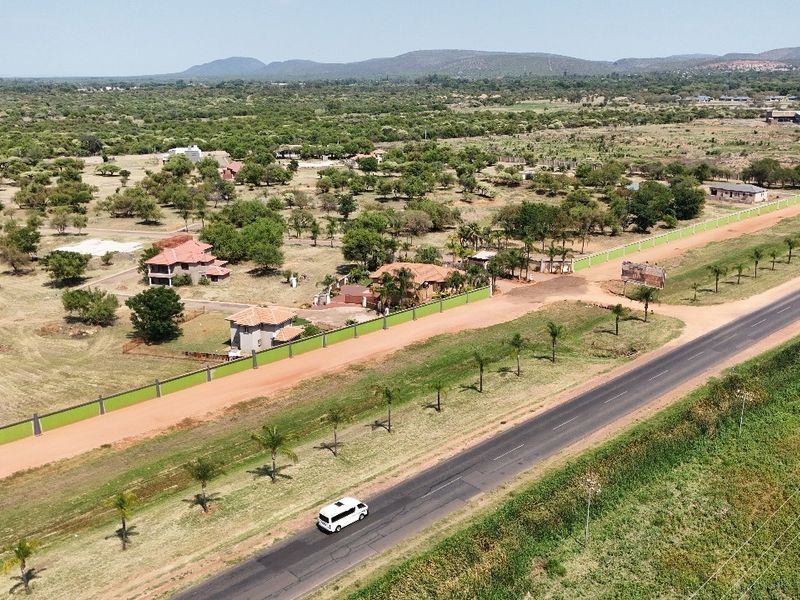 Aerial view of a residential vacant land plot featuring perimeter fencing and direct access to a paved main road in a rural setting.