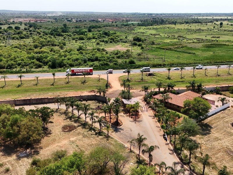 Aerial view of a residential property featuring a gated entrance, paved driveway, and surrounding landscaped grounds with a clear view of the adjacent road.