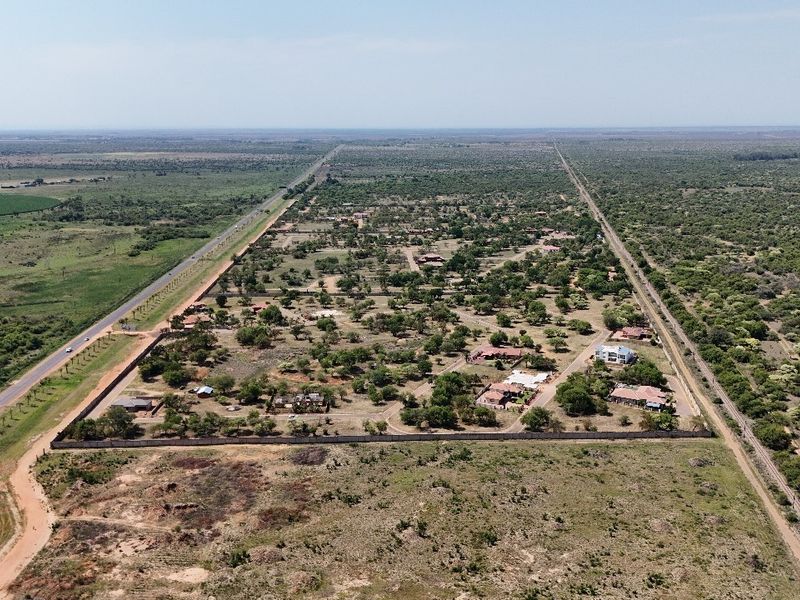 Aerial view of a residential land development featuring established plots, perimeter fencing, and proximity to major road and rail infrastructure.