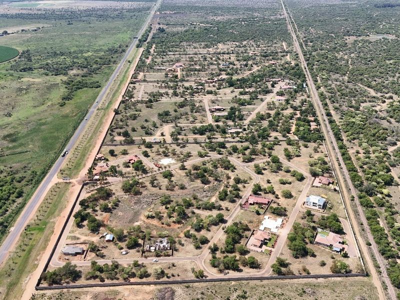 An aerial view of a residential estate development featuring established plots, internal road networks, and perimeter security fencing within a natural landscape.