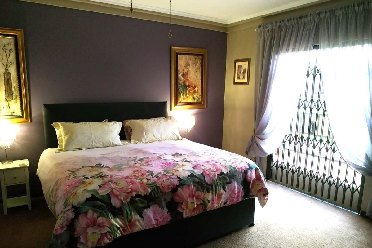 A bedroom featuring a dark accent wall, carpeted flooring, and a sliding door with a security gate leading to the exterior.