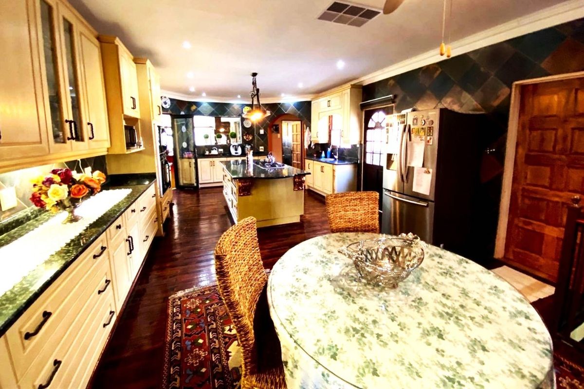 Spacious kitchen featuring a central island, granite countertops, wooden cabinetry, and integrated appliances, with an adjacent dining area.