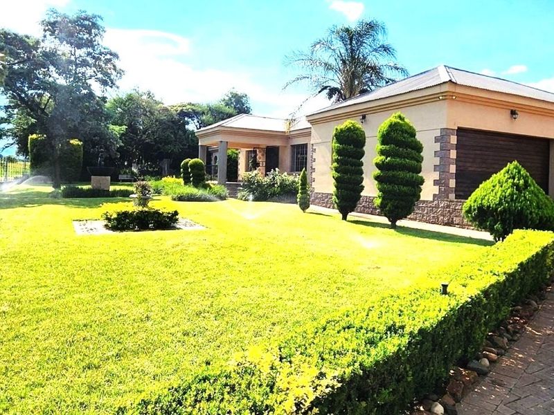A well-maintained exterior view of the small holding featuring a manicured lawn, landscaped garden, paved driveway, and double garage.