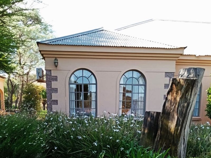Exterior view of the property featuring arched windows, stone corner detailing, and a corrugated metal roof set within a landscaped garden.