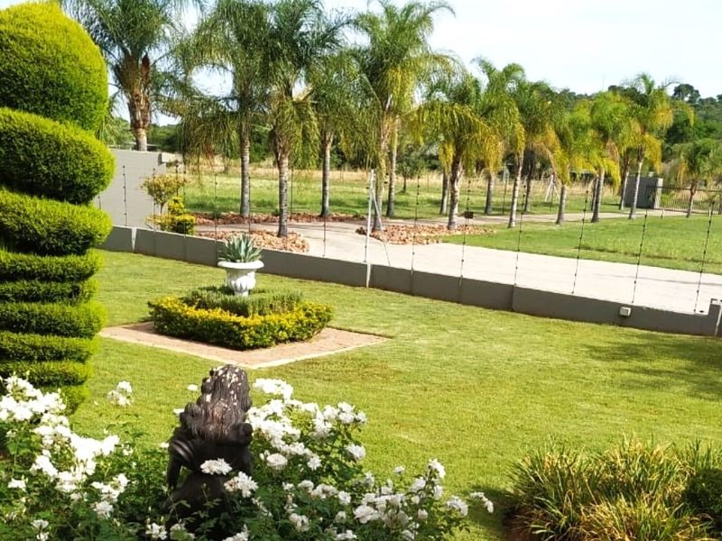 A well-maintained garden area featuring manicured lawns, established palm trees, and perimeter electric fencing on a concrete boundary wall.