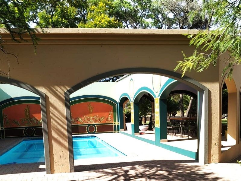Covered outdoor entertainment area featuring a swimming pool, arched architectural detailing, and decorative wall murals, ideal for hosting and relaxation.