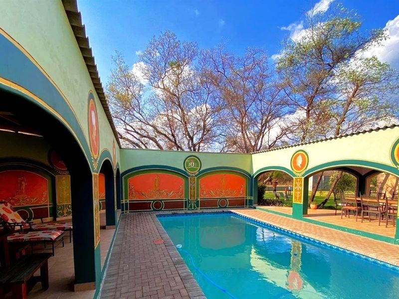A well-maintained outdoor pool area featuring decorative arched walls, paved surrounds, and a covered patio space, ideal for outdoor entertainment.