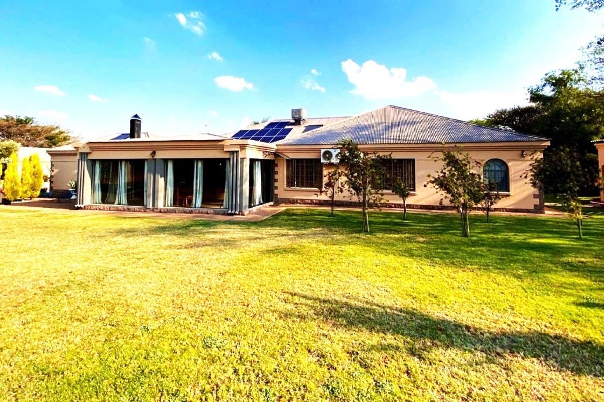 Rear view of the property featuring a spacious lawn, covered patio area, solar panels, and an external air conditioning unit.
