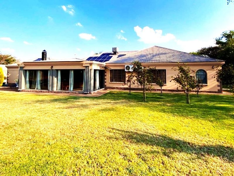 Rear view of the property featuring a spacious lawn, covered patio area, solar panels, and an external air conditioning unit.