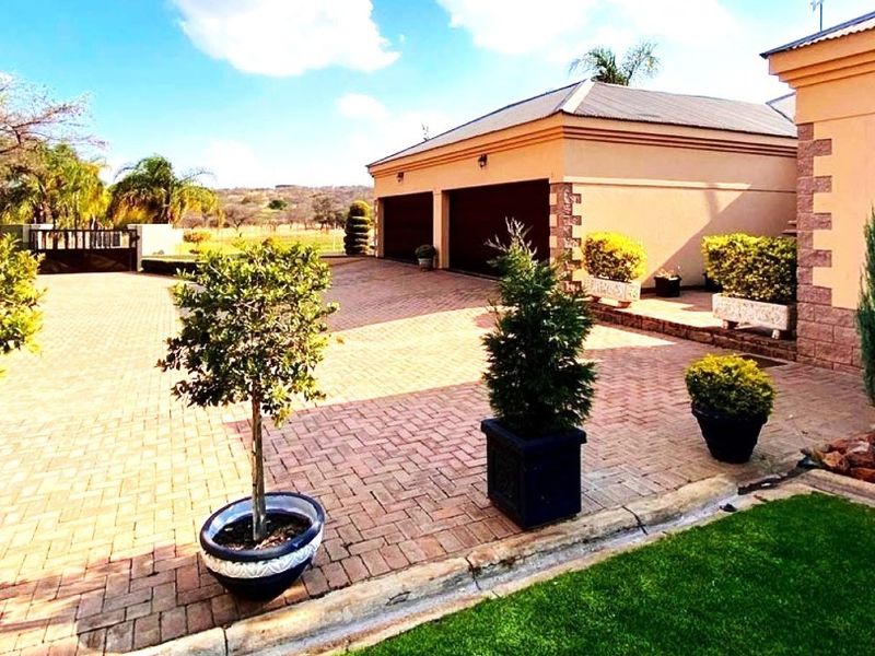 A well-maintained paved driveway leading to a double garage, featuring neat landscaping and established garden beds on a small holding property.